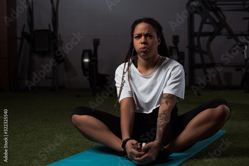  Tensed african american woman sitting with clenched hands on fitness mat