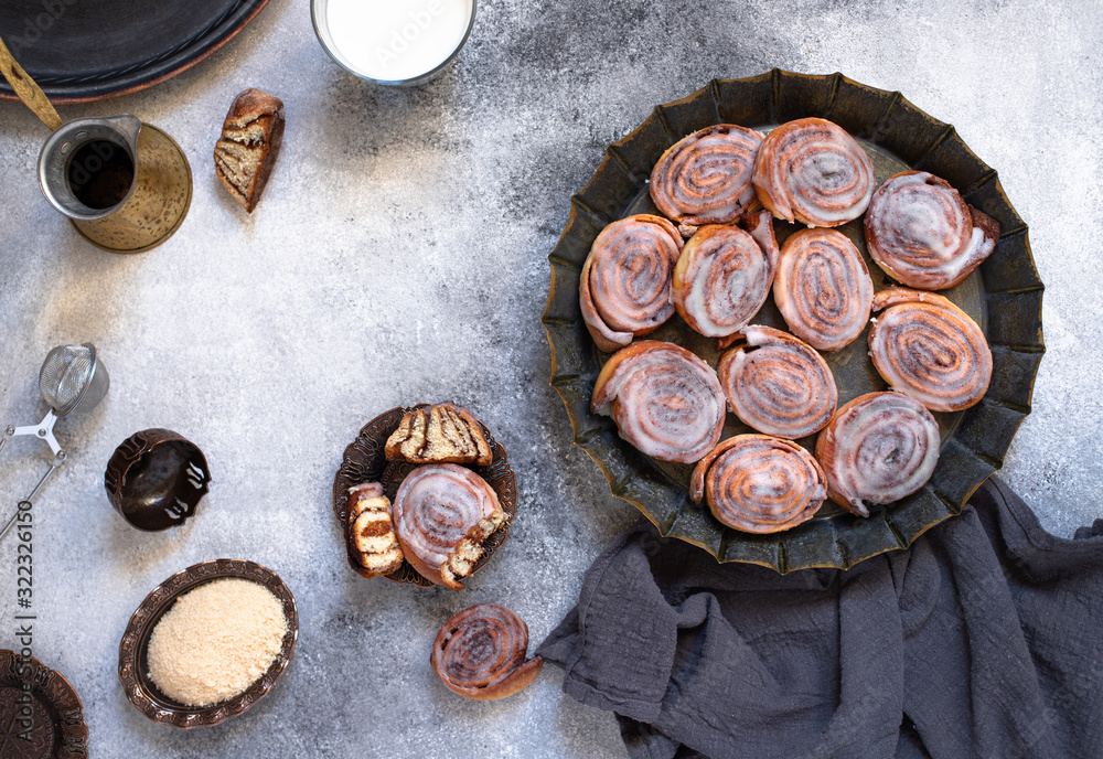 Cinnamon rolls or cinnabon with white cream glaze on a vintage plate, coffee, milk, brown sugar. Homemade traditional bakery dessert. Gray background, top view, copy-space Cinnamon rolls or cinnabon with white cream glaze on a vintage plate, coffee, milk, brown sugar. Homemade traditional bakery dessert. Gray background, top view, copy-space