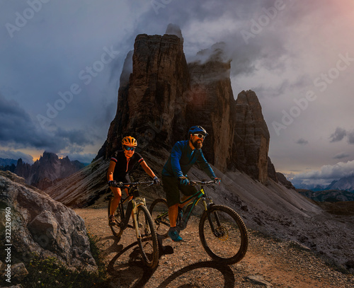 Couple cycling on electric bike, rides mountain trail. Woman and Man riding on bikes in Dolomites mountains landscape. Cycling e-mtb enduro trail track. Outdoor sport activity.