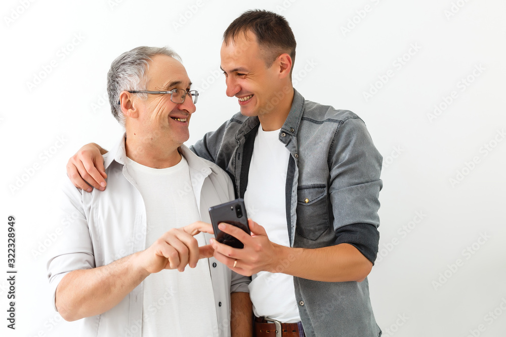 Happy two age generations men family old father embracing young grown adult son having fun enjoying using smart phone bonding watching funny social media video using mobile apps Happy two age generations men family old father embracing young grown adult son having fun enjoying using smart phone bonding watching funny social media video using mobile apps
