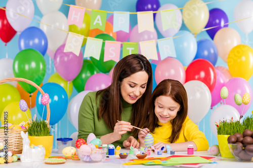 Portrait of nice attractive lovely creative tender cheerful cheery girls enjoying painting eggs mom mum teaching small little redhair sister