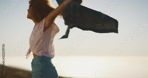 Carefree happy smiling african american woman spinning and dancing in the sun with a denim jacket, cheerful independent woman dancing at sunset outdoors photo