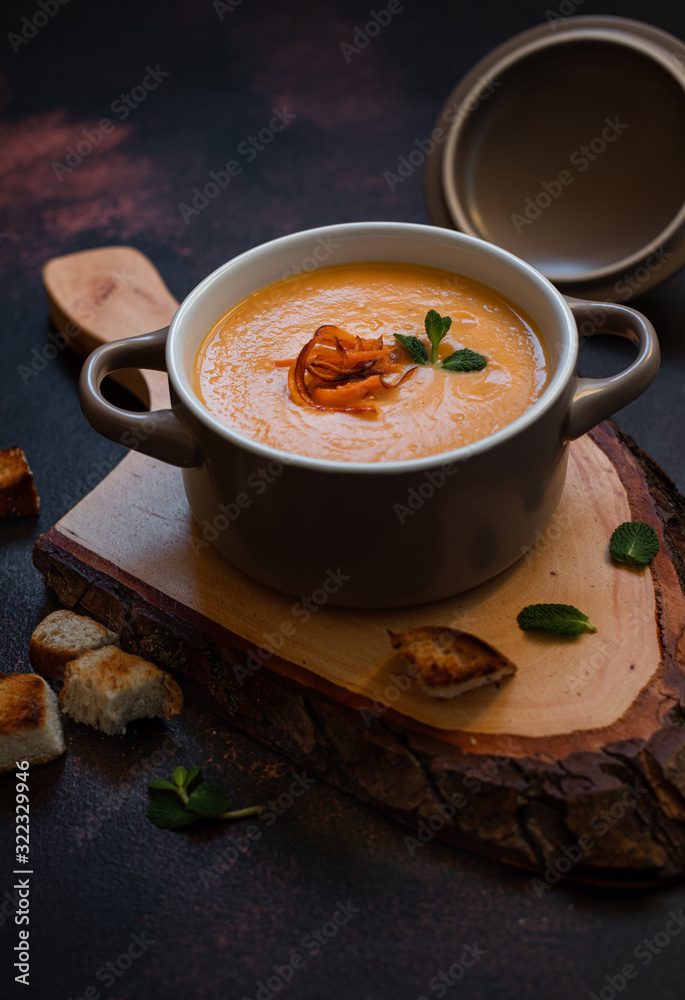 Cream sweet potato soup with sweet potato chips, breadcrumbs and herbs served in vintage copper plates on a vintage tray on a dark background. Vegetarian cream soup, healthy food. Close-up, copy space Cream sweet potato soup with sweet potato chips, breadcrumbs and herbs served in vintage copper plates on a vintage tray on a dark background. Vegetarian cream soup, healthy food. Close-up, copy space