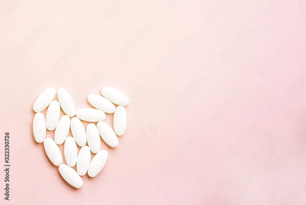 white heart from tablets and pills isolated on pink background with sunlight.