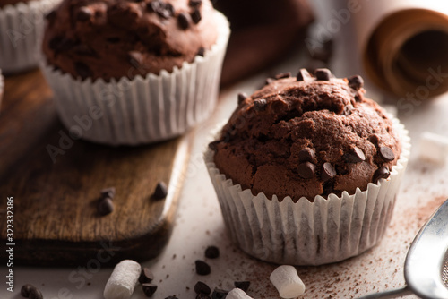 close up view of fresh chocolate muffins with marshmallow on wooden cutting board