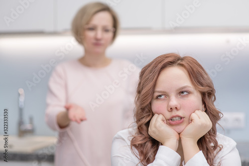 The teenage girl closed her eyes and closed her ears. Her mother in the background chastises her. Relationship problems, puberty photo