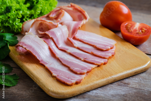 Raw sliced bacon on wooden board