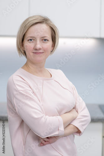 Free Download Young woman is standing in the kitchen smiling while looking at the camera - GFXLoad