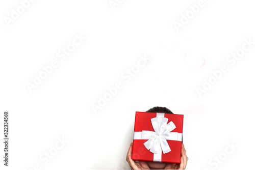 a young man holding a red present box on a white background. child covers his face with a box