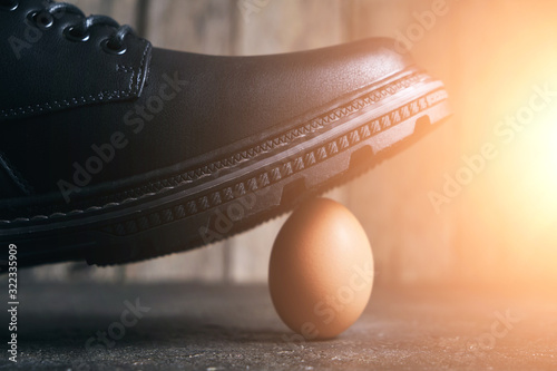 Fotografia Black boot steps on a fragile chicken egg