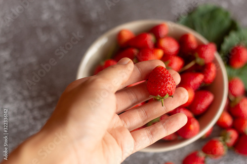 Young women hand catch fresh strawberries with green leave head in a white cup on white marble background.