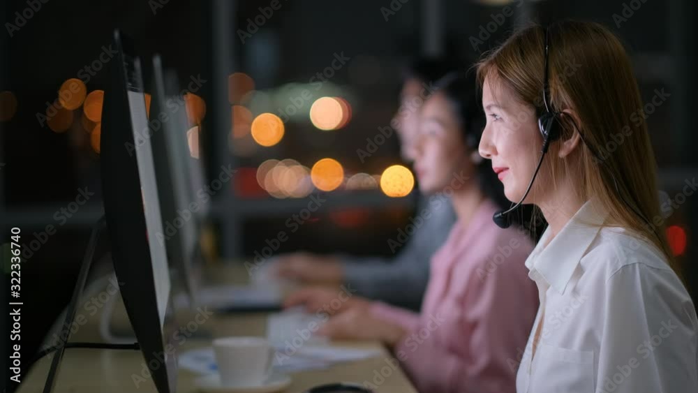 Pretty Asian operator girl work then look to the camera and smile during work with team at night. Pretty Asian operator girl work then look to the camera and smile during work with team at night.