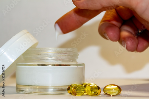 Face cream in a gold jar with gold capsules on a light background.