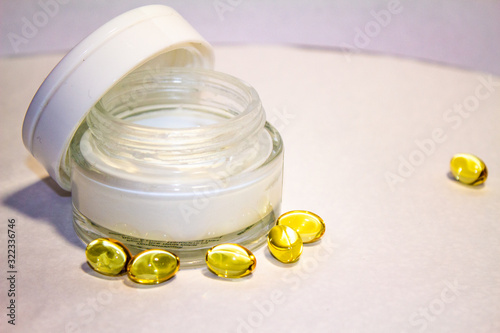 Face cream in a gold jar with gold capsules on a light background.