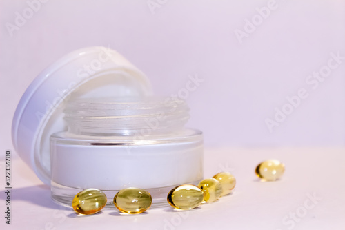 Face cream in a gold jar with gold capsules on a light background.