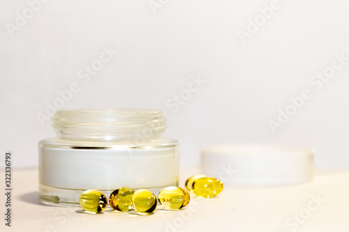 Face cream in a gold jar with gold capsules on a light background.