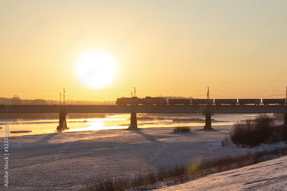 The train rushes along the railway bridge in the bright rays of the rising sun.