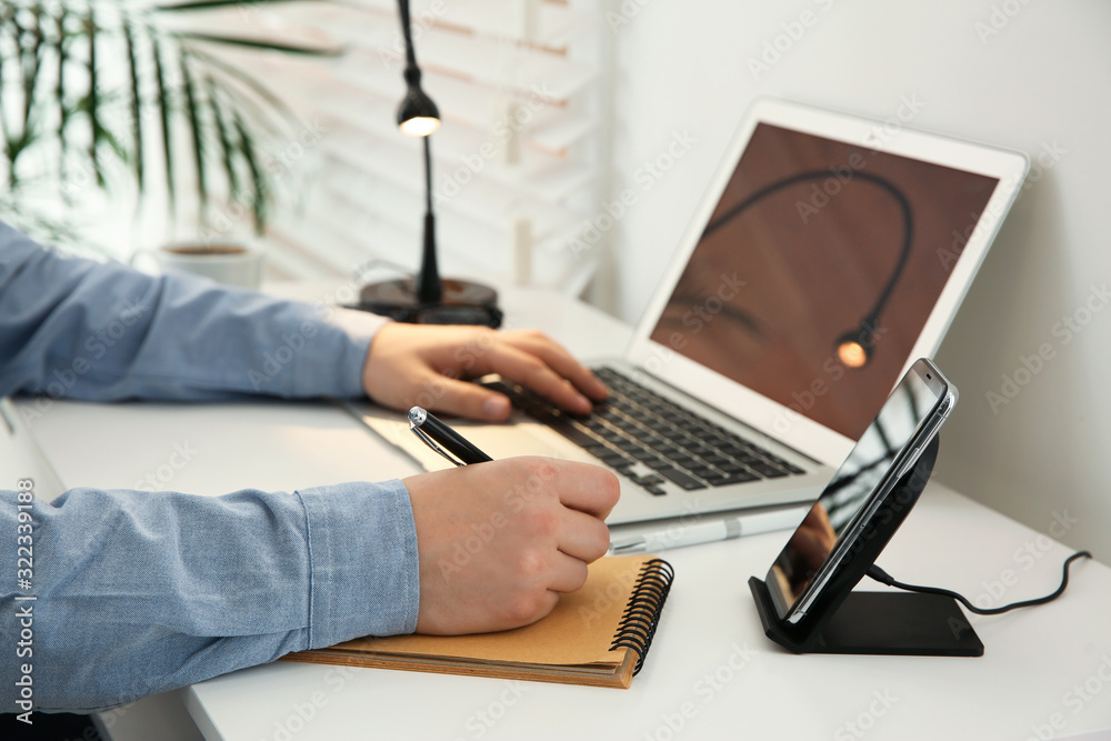 Fototapeta premium Man working at table while his mobile phone charging with wireless device