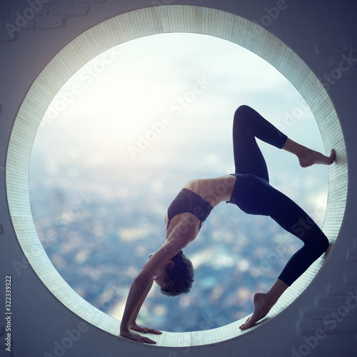 Beautiful sporty fit yogi woman practices yoga asana Eka Pada Urdhva Dhanurasana in a round window photo