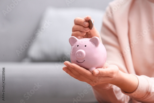 Woman putting coin into piggy bank at home, closeup. Space for text