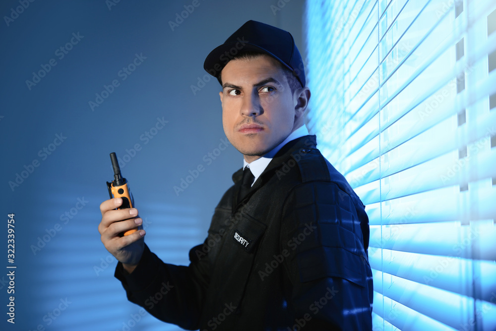 Professional security guard with portable radio set near window in dark ...