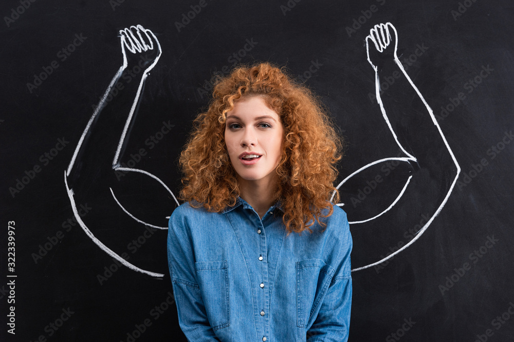 portrait of beautiful positive woman with strong muscular arms drawing on chalkboard