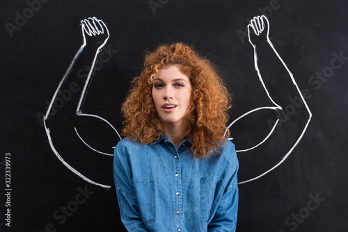 portrait of beautiful positive woman with strong muscular arms drawing on chalkboard