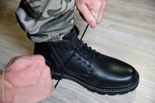 Man in a military uniform ties the laces on his black shoes.