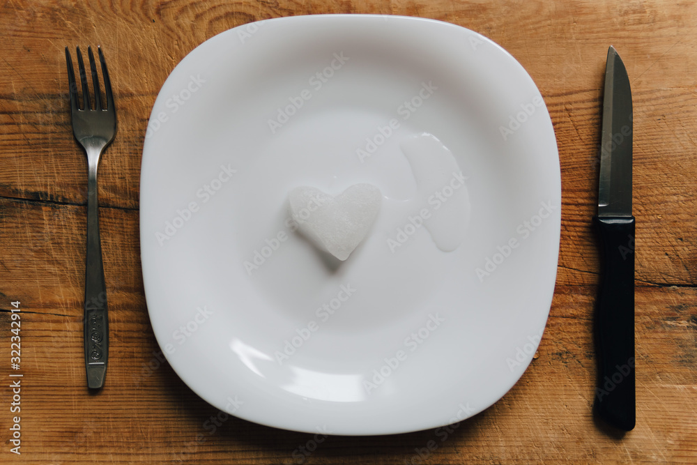 A snowy heart melts on a white plate. Heart shaped snow on a saucer. Ice in frosty weather. Melted water is collected in a small puddle. Wooden background. Love on valentine's day concept A snowy heart melts on a white plate. Heart shaped snow on a saucer. Ice in frosty weather. Melted water is collected in a small puddle. Wooden background. Love on valentine's day concept