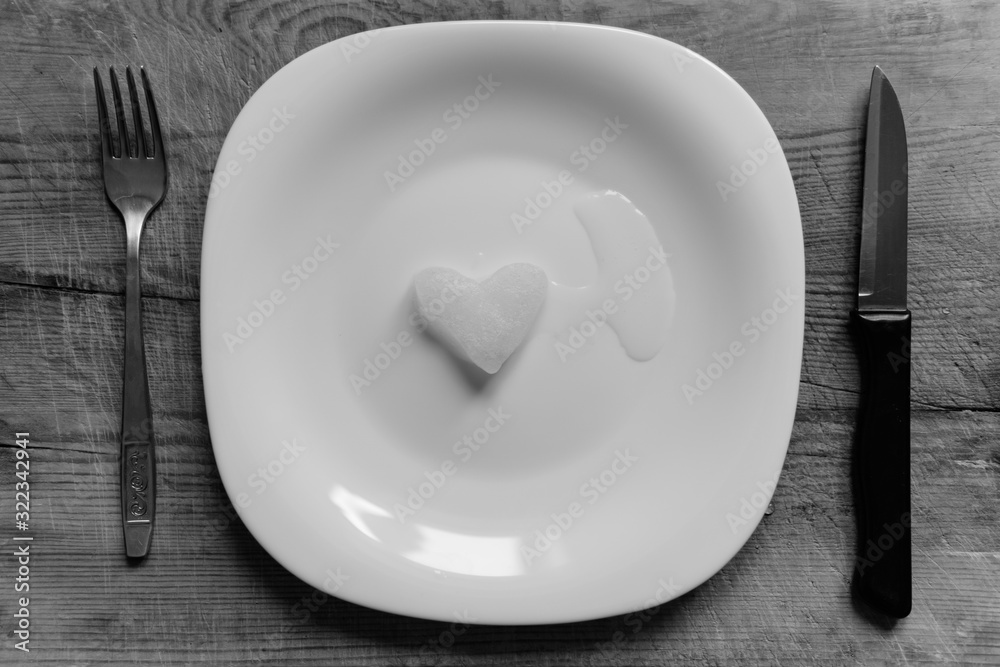 A snowy heart melts on a white plate. Heart shaped snow on a saucer. Ice in frosty weather. Melted water is collected in a small puddle. Wooden background. Love on valentine's day concept A snowy heart melts on a white plate. Heart shaped snow on a saucer. Ice in frosty weather. Melted water is collected in a small puddle. Wooden background. Love on valentine's day concept