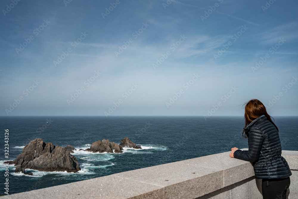 Woman watching the sea and waves breaking on the rocks