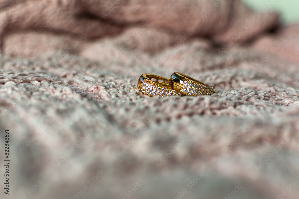 Obraz premium Gold modern earrings of large size, completely covered with small white transparent stones cubic Zirconia, creating artificial gold in a fashionable piece of jewelry on a velvet pink background