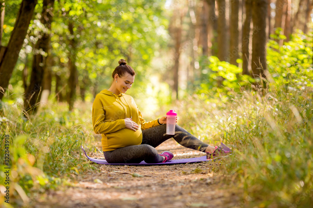 young pregnant woman doing yoga in the summer in the forest,Pregnant practices yoga outdoors. Prenatal Yoga and Fitness Future mom doing stretching exercises. young pregnant woman doing yoga in the summer in the forest,Pregnant practices yoga outdoors. Prenatal Yoga and Fitness Future mom doing stretching exercises.