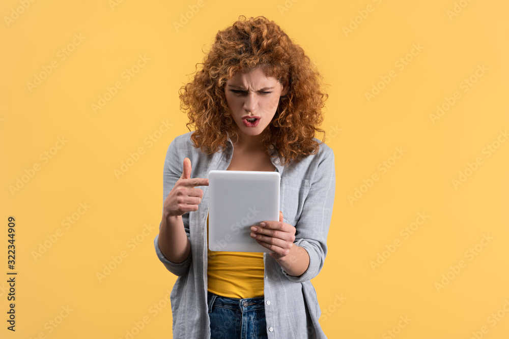 aggressive girl pointing and shouting at digital tablet, isolated on yellow