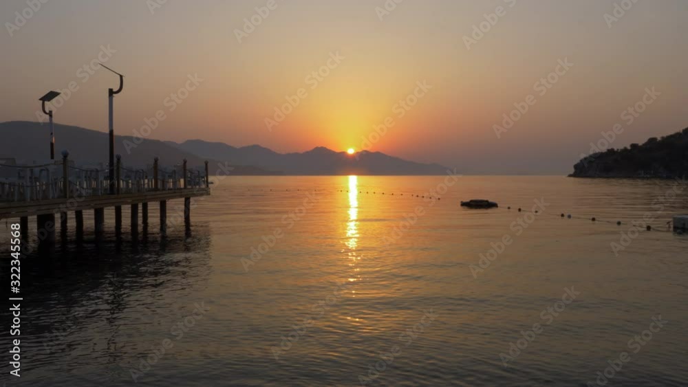 Beautiful morning sunrise on mountain and sea landscape. Golden sun rising over mountain silhouette and calm sea timelapse. Morning dawn on beach pier and ocean water background Beautiful morning sunrise on mountain and sea landscape. Golden sun rising over mountain silhouette and calm sea timelapse. Morning dawn on beach pier and ocean water background