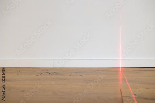 Laser meter on white wall and parquet in new apartment. Precision measurements on building renovation sites for architects and carpenters and bricklayers. Red laser beam on wall and copyspace © PAOLO