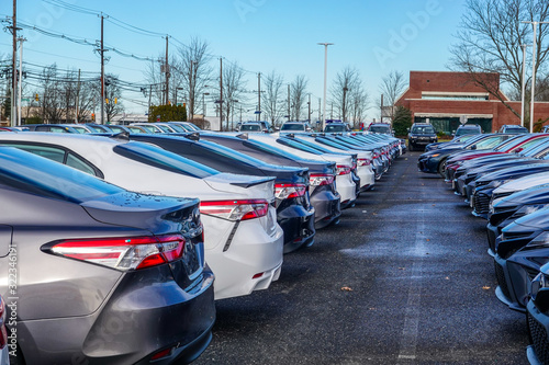 View of the back of a row of various colored new cars in a parking lot photo