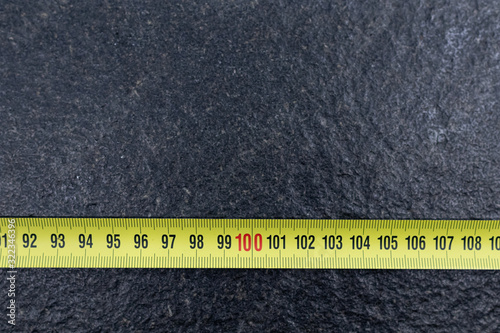 One meter on Yellow tape measure on black stone. Measurement tools for construction and carpentry, tools for home renovation and measurements. flexible meter showing red numbers with 100 in the center photo