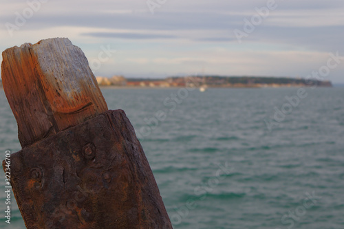 Rusty base with weathered broken wooden beam in foreground. Soft background with seaside. 