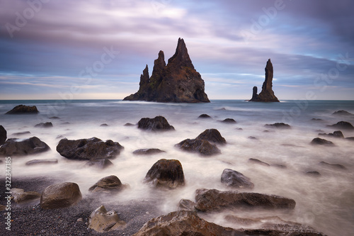 Famous tourist landscape with basalt rock formations Troll toes (Trolls fingers) on black beach. Ocean waves flow around stones. Reynisdrangar, Vik, Iceland, Atlantic Ocean, Europe. Travel postcard.