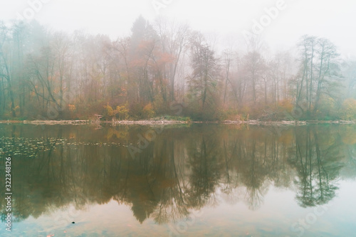 Autumn trees reflected in the waters of a foggy lake