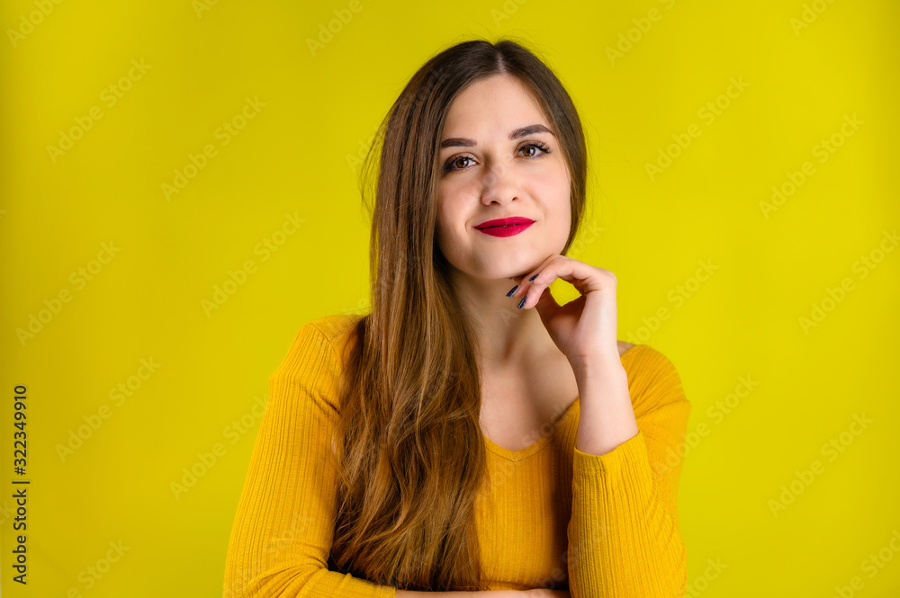 Portrait of a pretty brunette girl with long hair with a smile in a yellow sweater on a yellow background smiles and shows positive emotions Portrait of a pretty brunette girl with long hair with a smile in a yellow sweater on a yellow background smiles and shows positive emotions