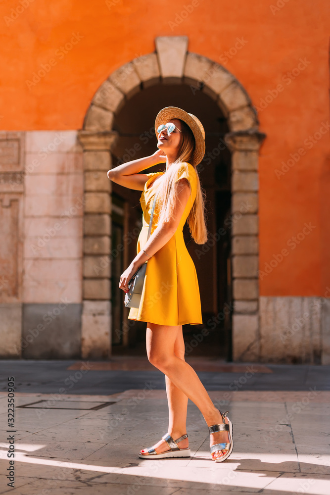 A beautiful girl in a yellow dress poses in front of the arch of