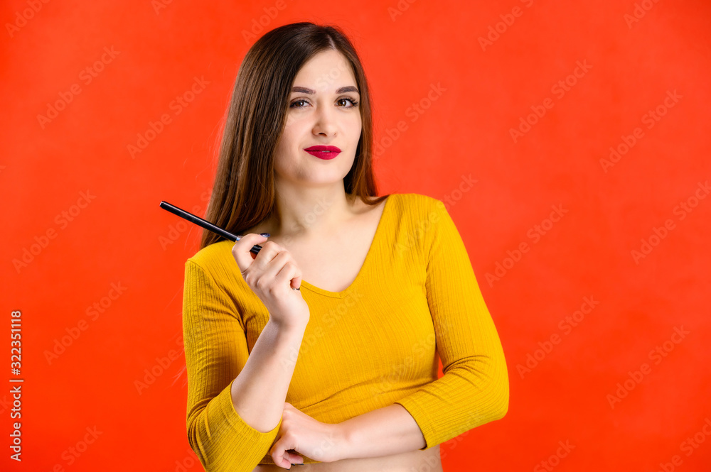 nice brunette girl with long hair with a smile with a pen in her hands in a yellow sweater is happy over a red background smiling and showing positive emotions nice brunette girl with long hair with a smile with a pen in her hands in a yellow sweater is happy over a red background smiling and showing positive emotions