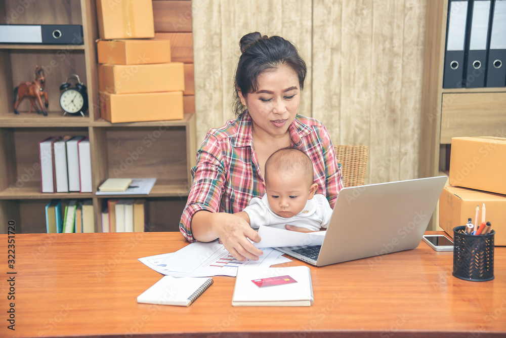 Pretty young single mom working at home on a laptop computer while holding her baby girl sitting on her lap enjoying watching mother working. Pretty young single mom working at home on a laptop computer while holding her baby girl sitting on her lap enjoying watching mother working.