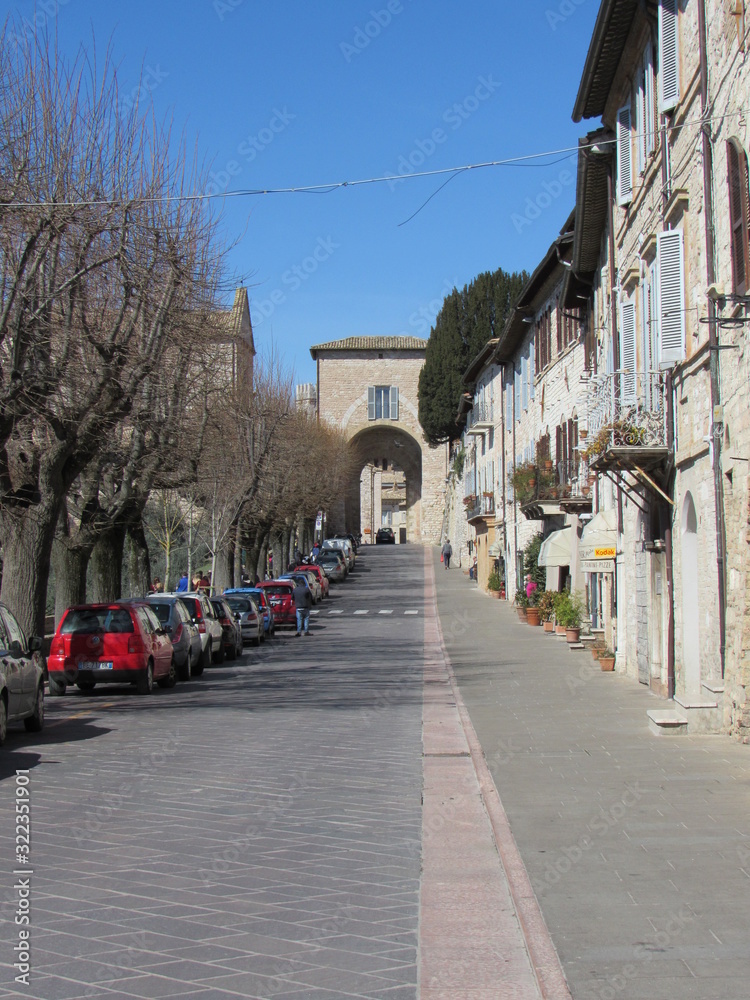 View down the street in Assisi, Italy with unrecognizable tourists and locals on a sunny day with blue sky
