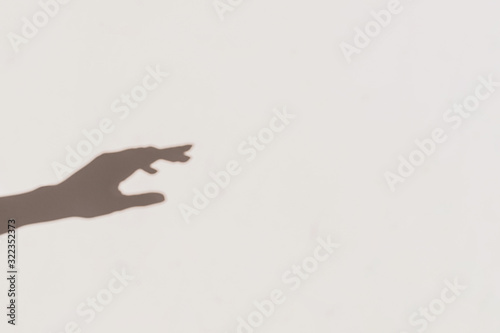 Grey shadows of one reaching hand on the wall. Abstract blurred effect.