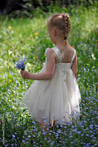 Kleines Mädchen mit Blumenstauss, weißem Kleid auf Blumenwiese im Frühling