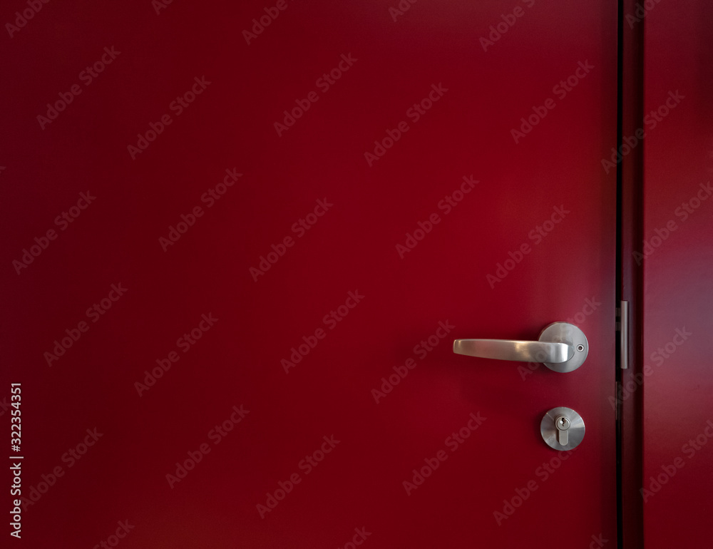 Obraz premium Semi-abstract close-up of part of a red door with metal handle and lock in natural light