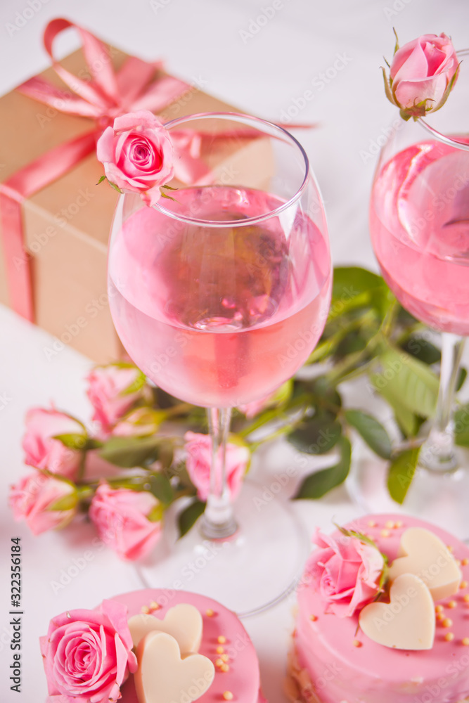 Two glasses with pink grape wine with rose flowers and mini cakes. Romantic dinner concept.